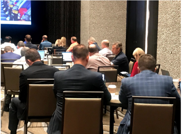 Attendees sit in chairs facing a screen at the front of a room.