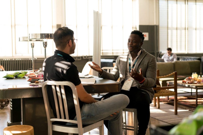 Two men sit at a table having a conversation.